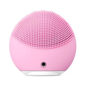 Pink silicone facial cleansing brush with densely packed soft bristles and a small front port for charging or 연결.
