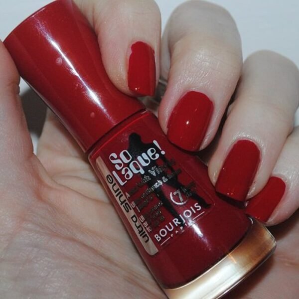 Hand holding Bourjois So Laque! red nail polish bottle with red nails visible on the fingers.