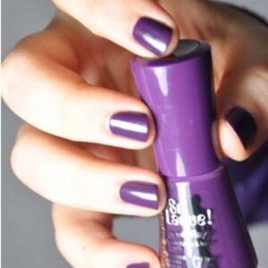 Close-up of a hand with purple nail polish holding a purple lipstick tube.