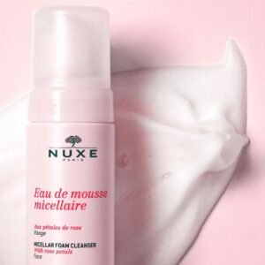 NUXE Paris pink bottle of micellar foam cleanser for the face, with rose-petal accents and a swirl of foam nearby on a pink backdrop.