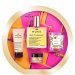 Nuxe gift set with multiple beauty products including Huile Prodigieuse oil bottle and creams on a bright pink and gold background