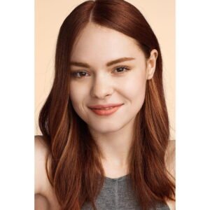 Portrait of a smiling woman with long auburn hair against a peach background, cropped at shoulders.