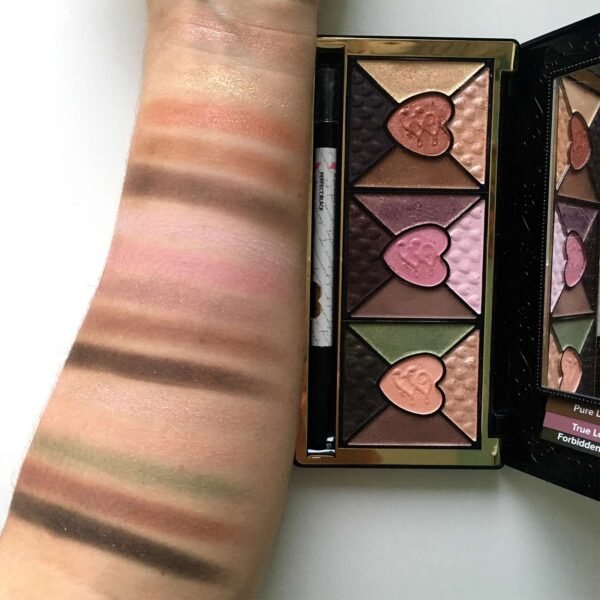 Arm swatches of shimmery peach, pink, and brown makeup next to a heart-shaped-embossed palette with mirrored lid.