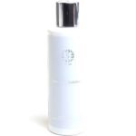 White cylindrical skincare bottle with a shiny silver cap, embossed floral logo and label reading 'Secret' and 'Soin Doux Exfoliant'.