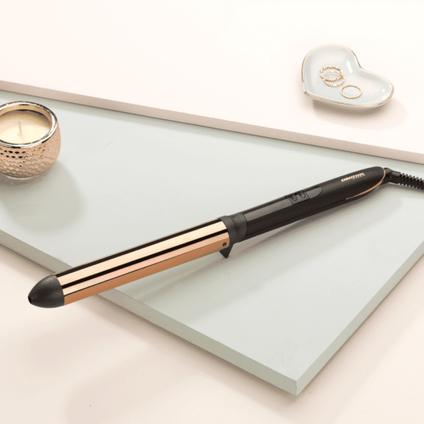 Gold-accented curling wand resting on a pale mint surface with a heart-shaped jewelry dish nearby.
