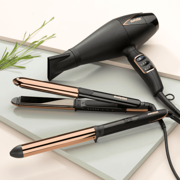 Black and rose-gold BaByliss hair styling set: dryer, two flat irons, and curling wand on a glass surface.