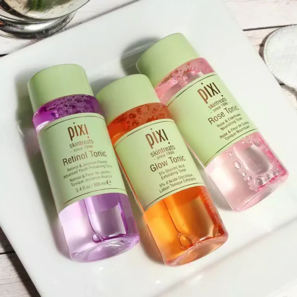 Three Pixi skintreat bottles—Retinol Tonic (purple), Glow Tonic (orange), and Rose Tonic (pink)—on a white plate.