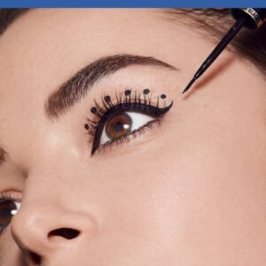 Close-up of an eye with bold eyeliner and mascara, eyebrow brushed in place, and a makeup tool near the brow.