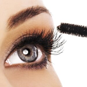 Close-up of a blue-gray eye with a mascara wand brushing the upper lashes